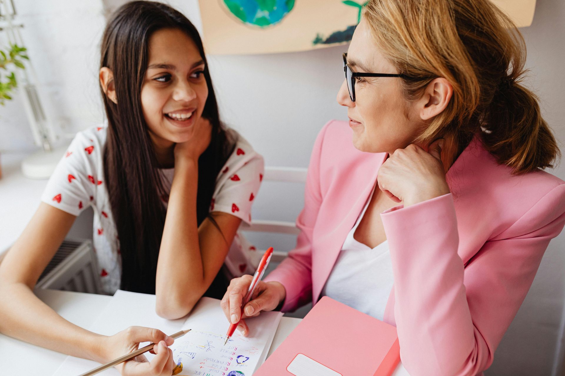 A woman in a pink jacket is sitting at a table with a young girl.