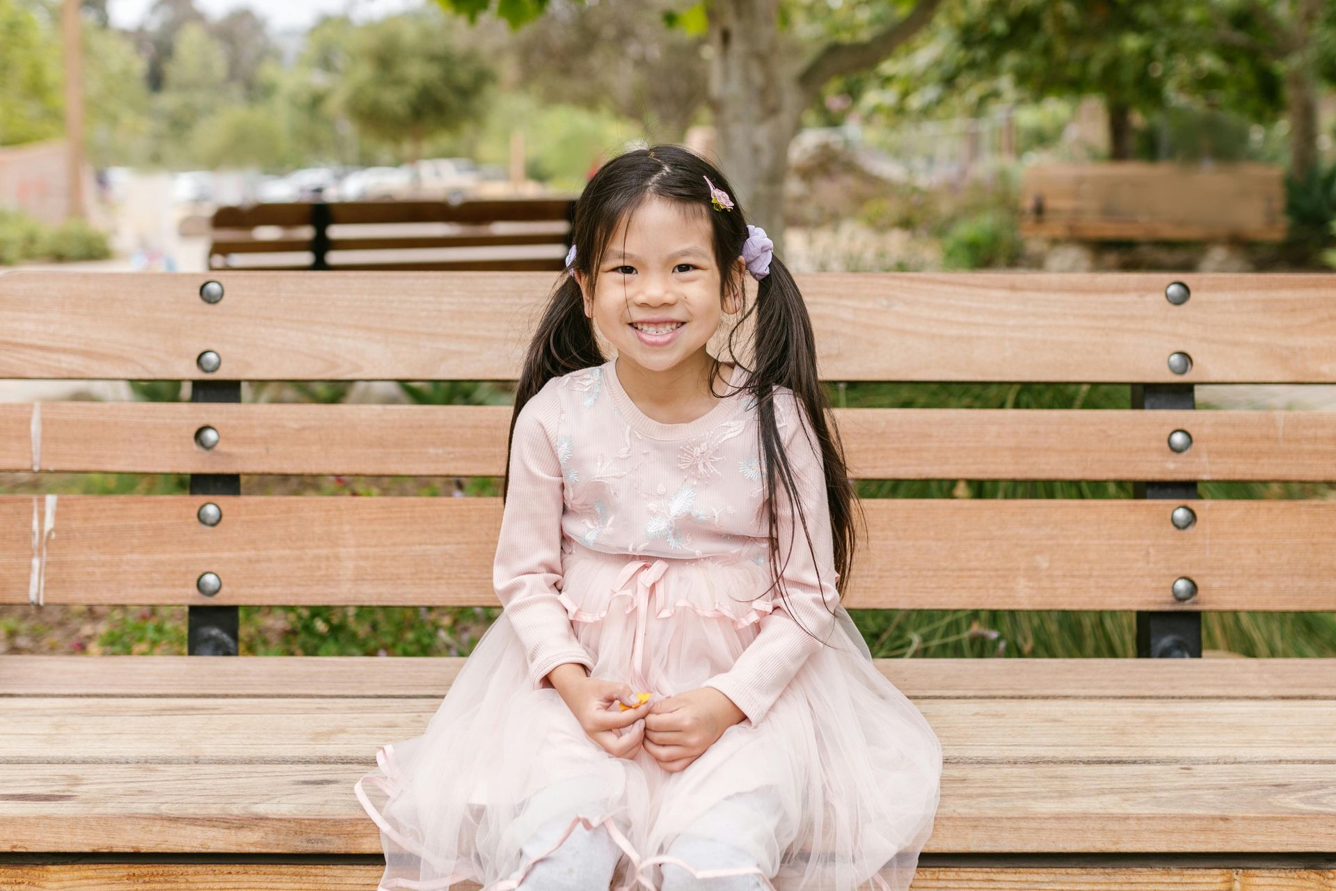 A little girl is sitting on a wooden bench in a park.