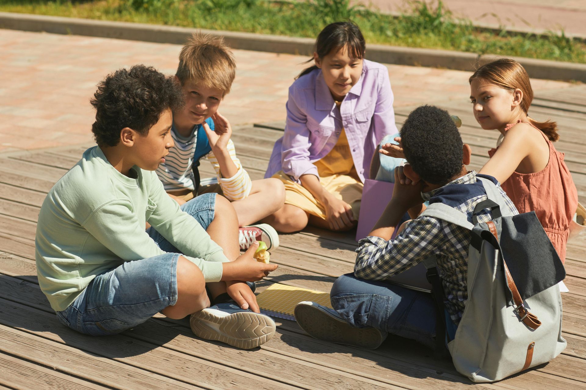 A group of diverse children sitting in a circle outdoors, talking.