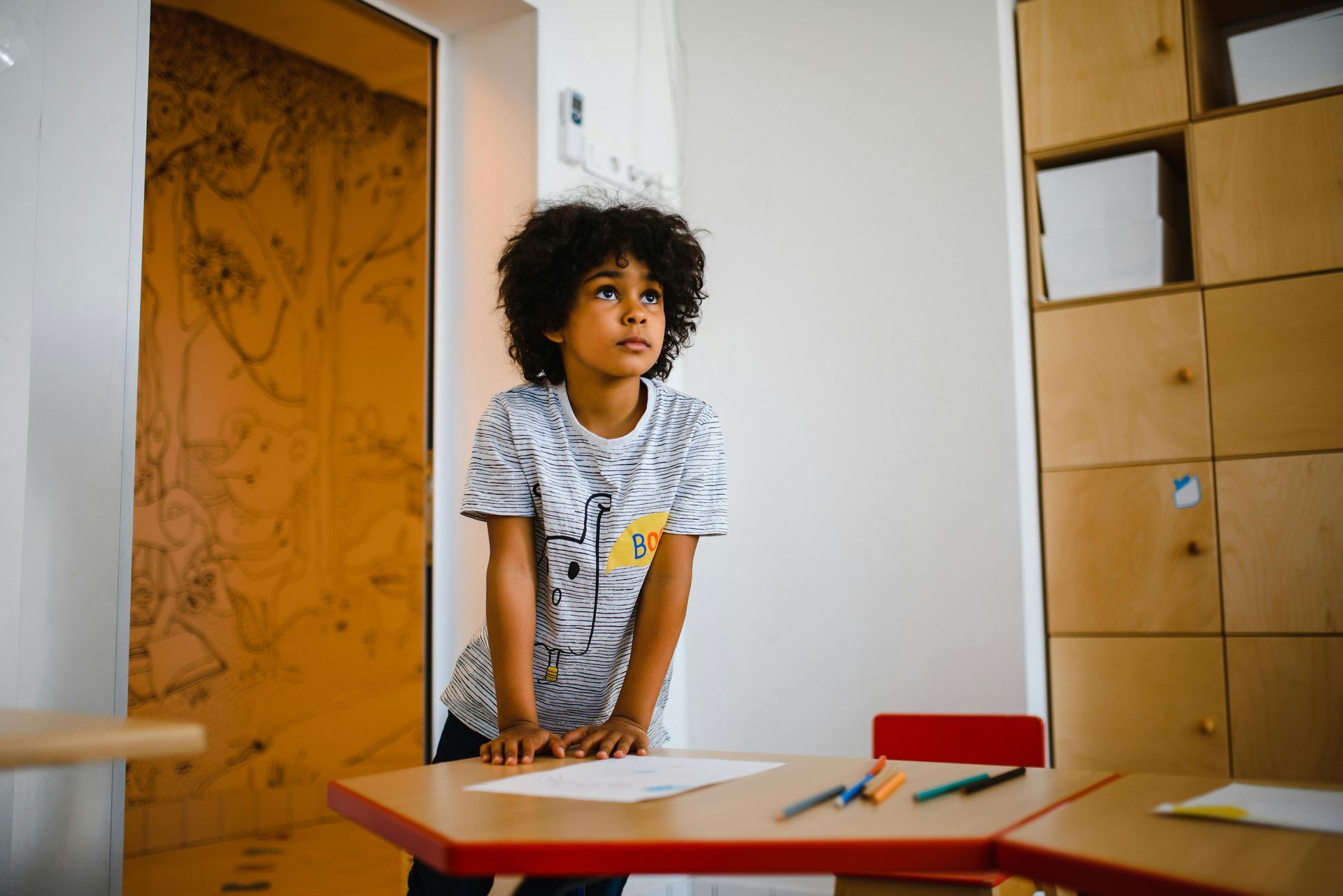 A young boy is standing at a desk in a classroom.