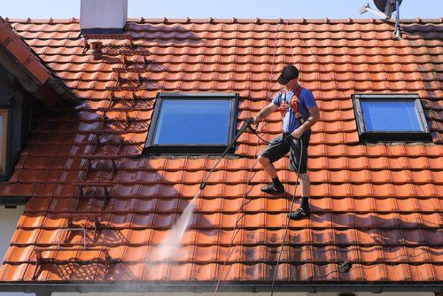Man on roof cleaning with high pressure hose