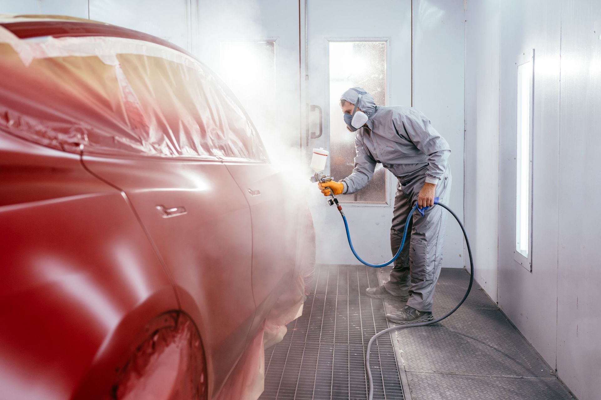 Person in Protective Suit Painting a Red Car | Peak Customs and Collision Inc