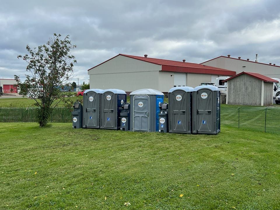 A row of portable toilets are lined up in a grassy field.