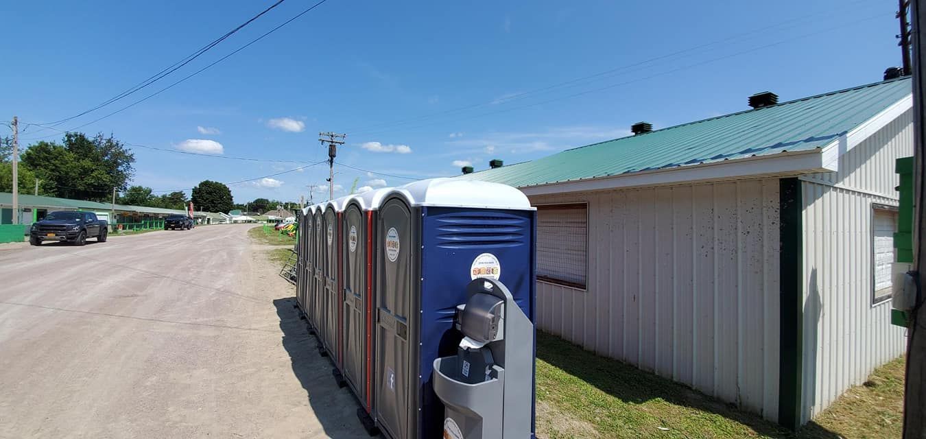 A row of portable toilets are parked on the side of a dirt road.