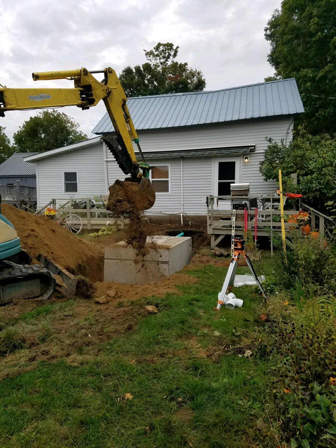 A yellow excavator is digging a hole in front of a house.