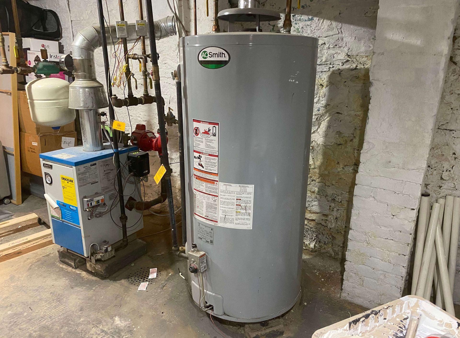 A water heater is sitting in a basement next to a boiler.