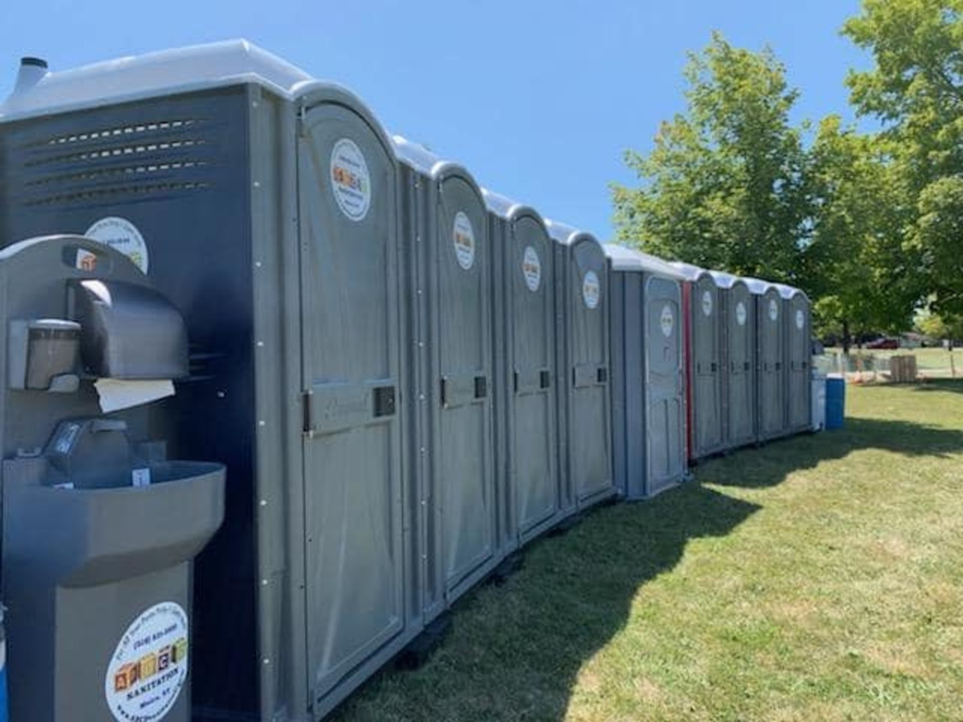 A row of portable toilets are lined up in a grassy field.