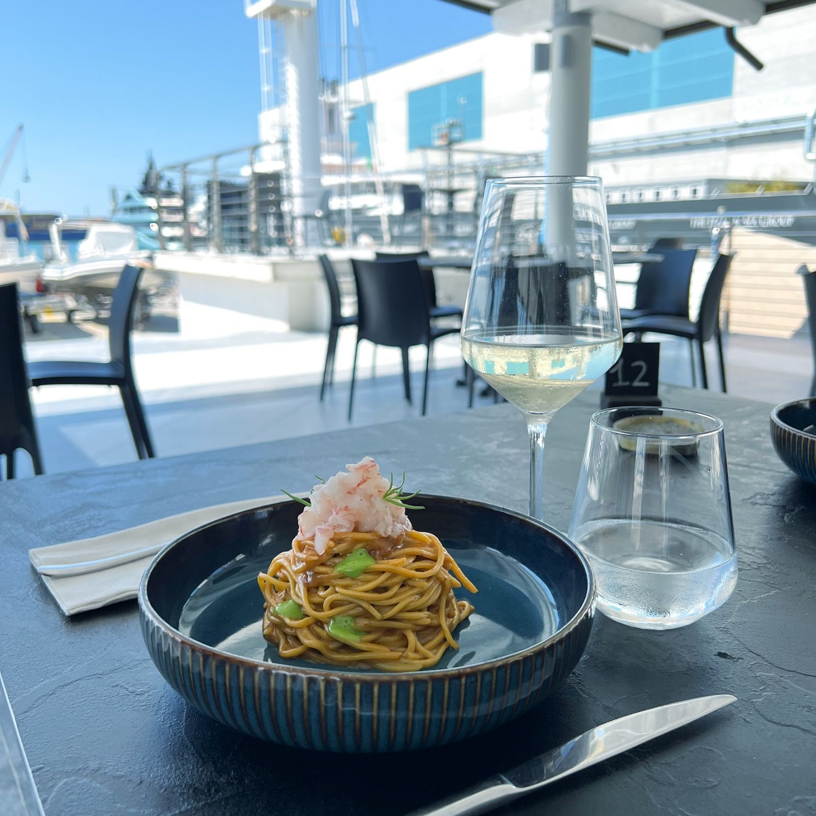 Una ciotola di spaghetti è appoggiata su un tavolo accanto a un bicchiere di vino