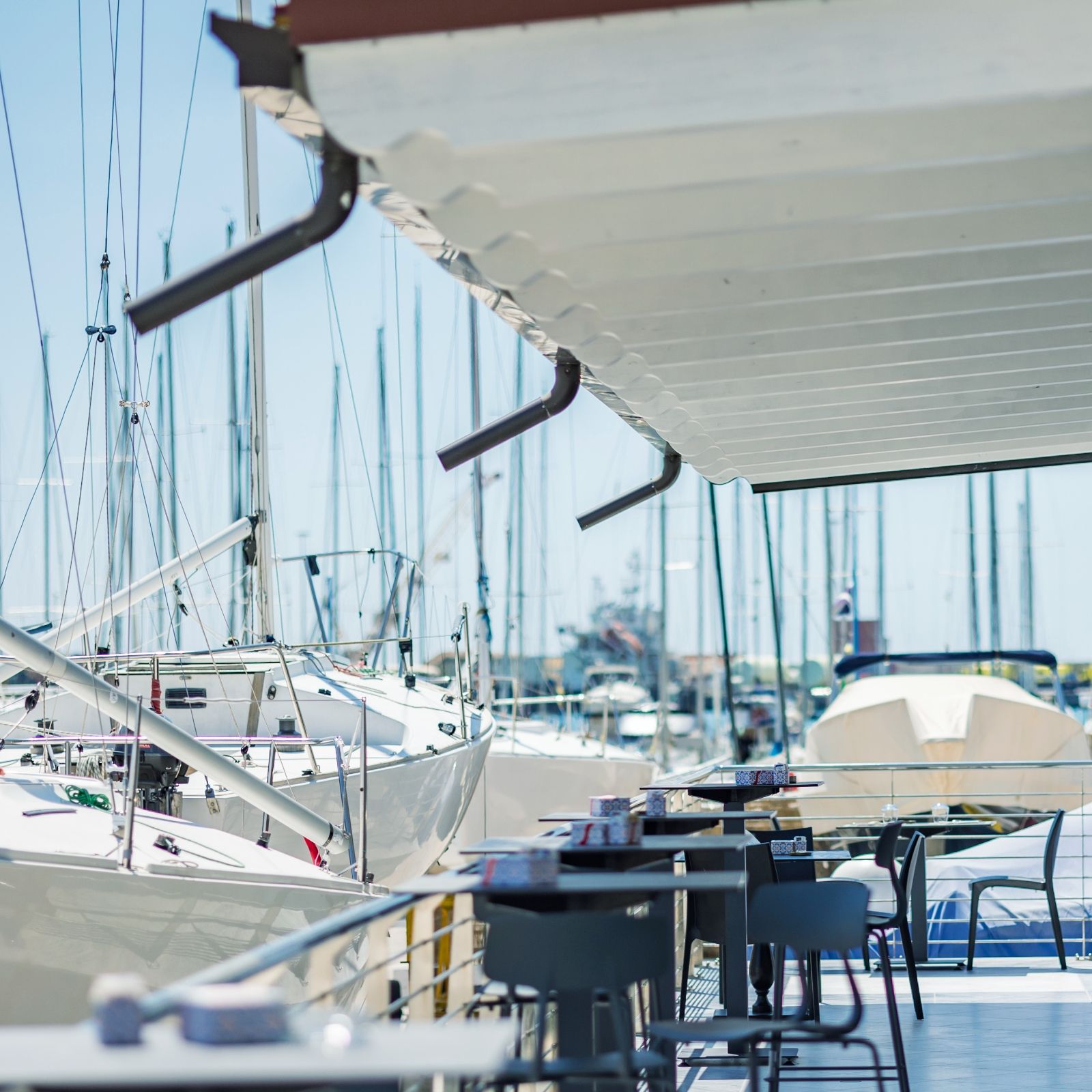 Una fila di tavoli e sedie in un porto turistico con barche sullo sfondo.