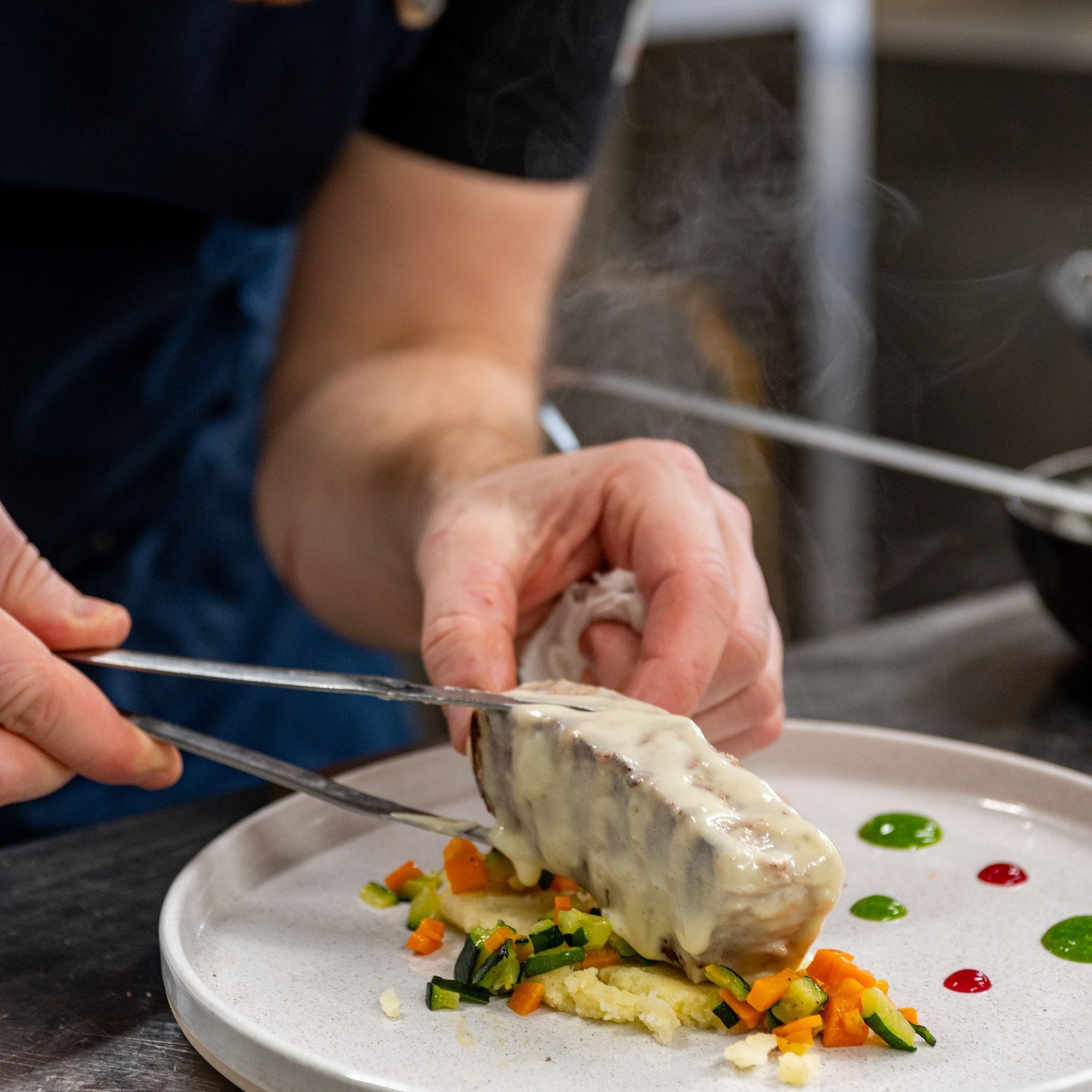 Una persona sta tagliando un pezzo di carne su un piatto con delle verdure.