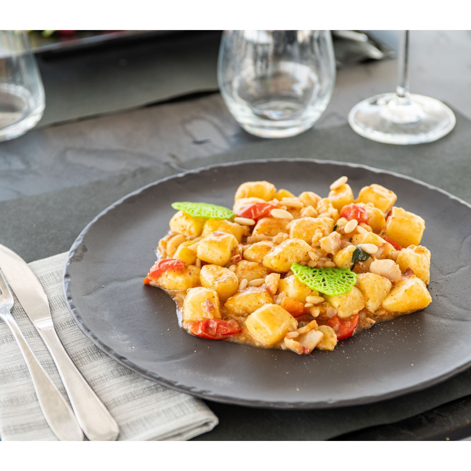 Un piatto nero con gnocchi e verdure su un tavolo.