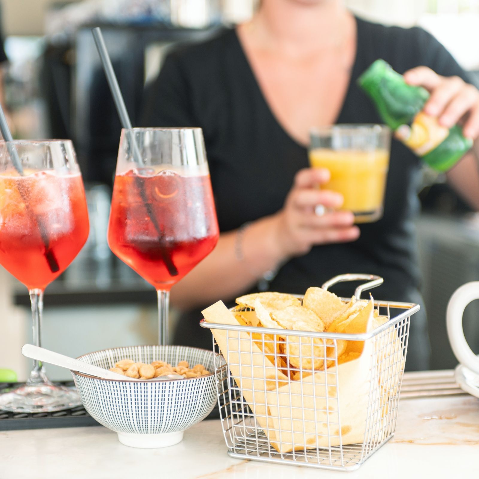 Una donna sta versando un drink in un bicchiere accanto a un cestino di patatine