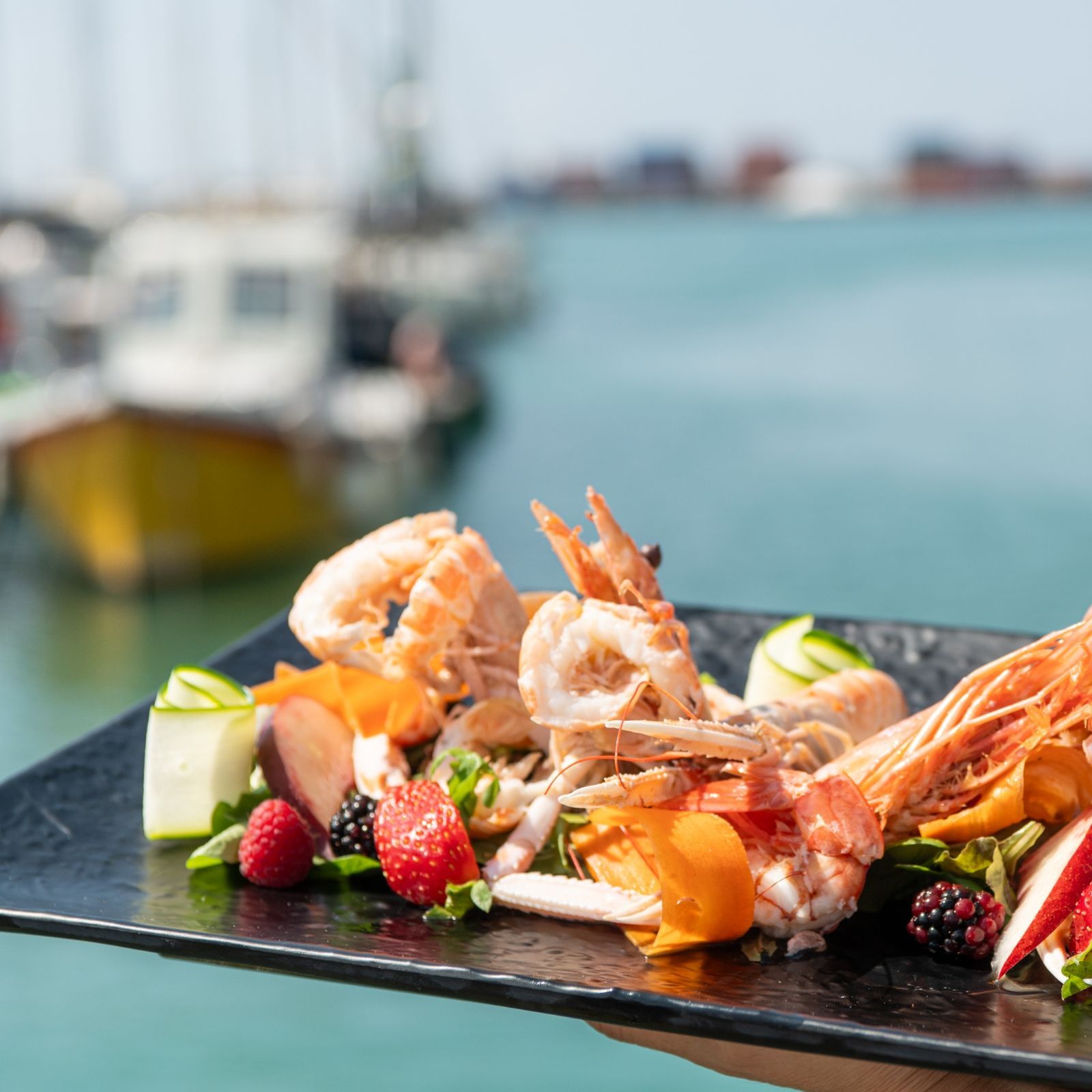 Una persona tiene in mano un piatto di cibo con delle barche sullo sfondo