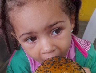 Uma menina está comendo um pão com sementes de gergelim.