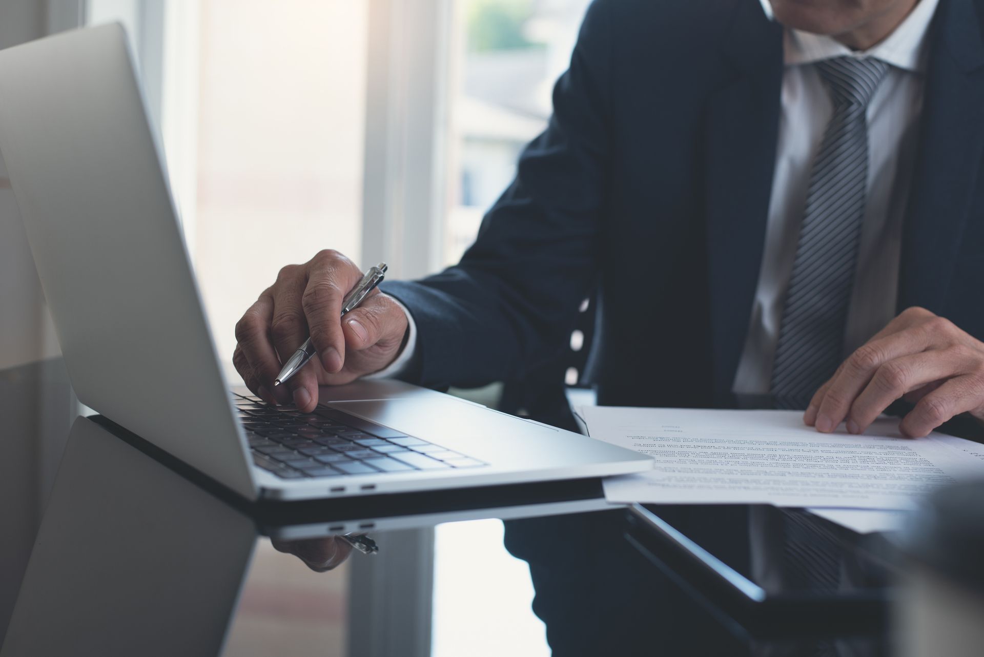 a man in a suit and tie is sitting at a desk using a laptop computer .