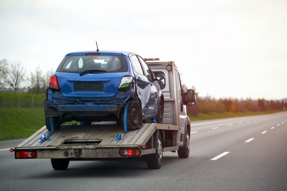 A Blue Car Is Being Towed by A Tow Truck on A Highway  — Bakers Creek Wreckers In Gracemere, QLD
