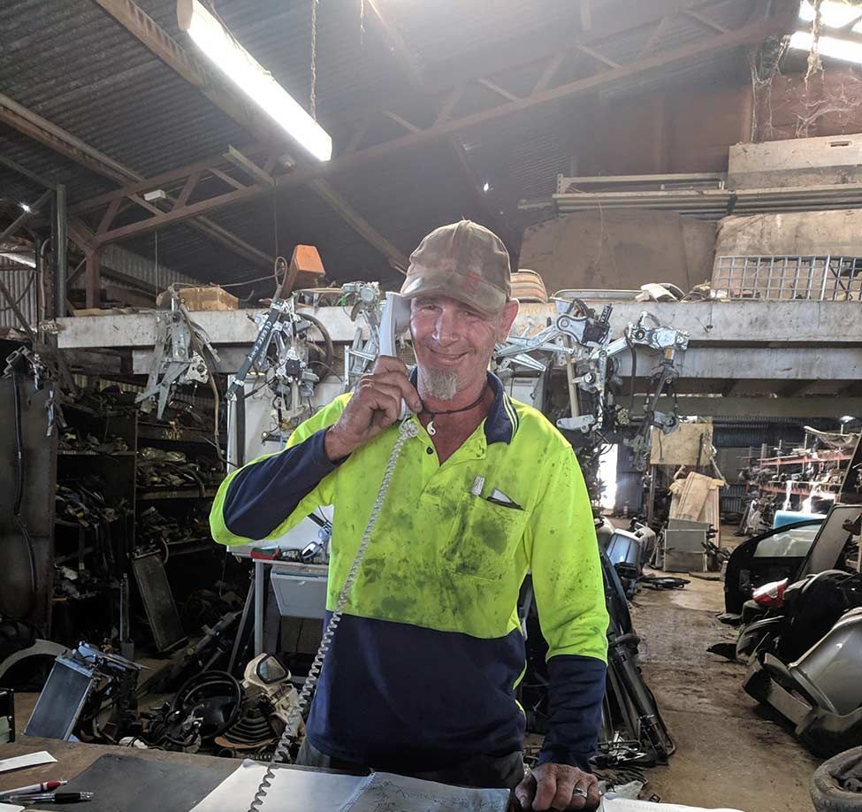 A Man Is Sitting at A Counter in A Garage Talking on A Cell Phone — Bakers Creek Wreckers In Bakers Creek, QLD