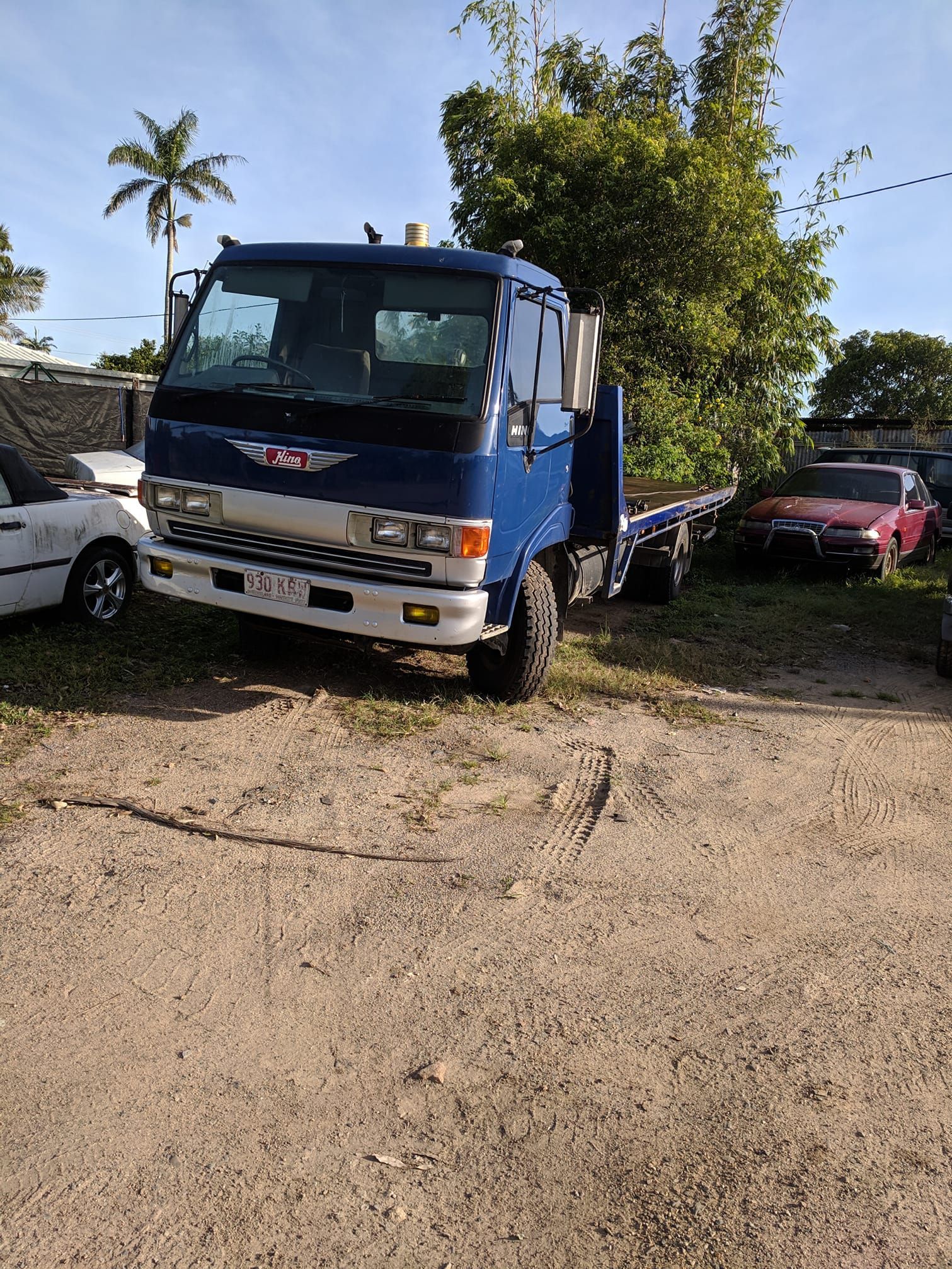 A Blue Truck Is Parked In A Dirt Lot Next To A White Car — Bakers Creek Wreckers In Bakers Creek, QLD