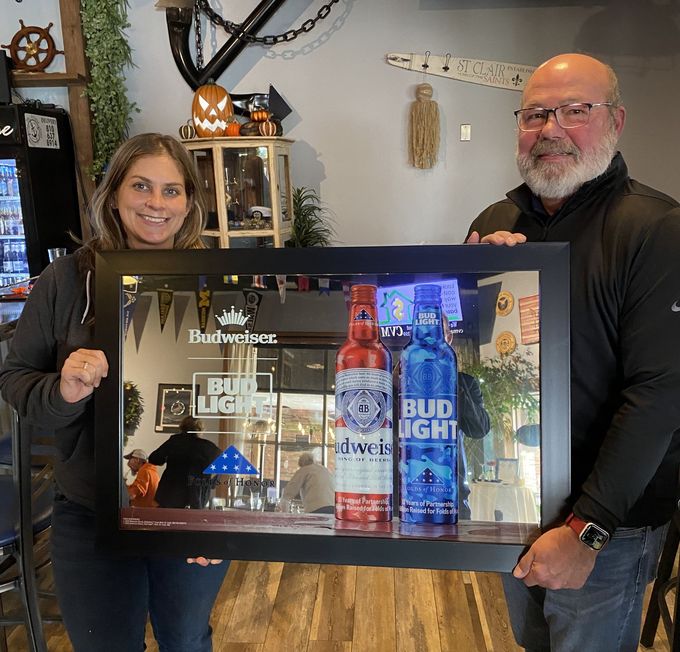 A man and a woman are holding a framed picture of bud light bottles