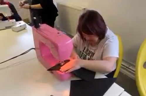 a woman is sitting at a table using a pink sewing machine .