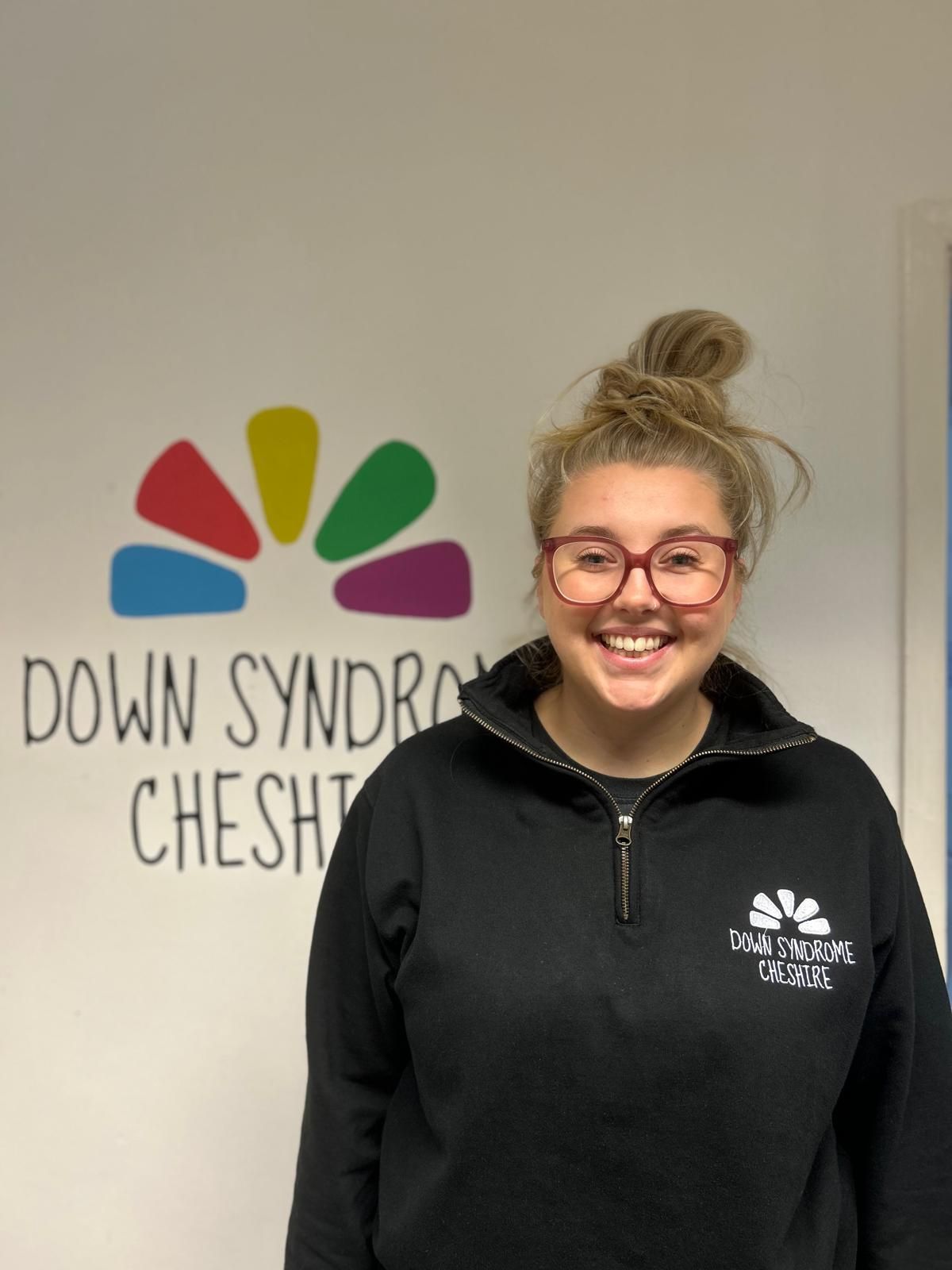 a woman wearing glasses and a black hoodie is smiling for the camera .