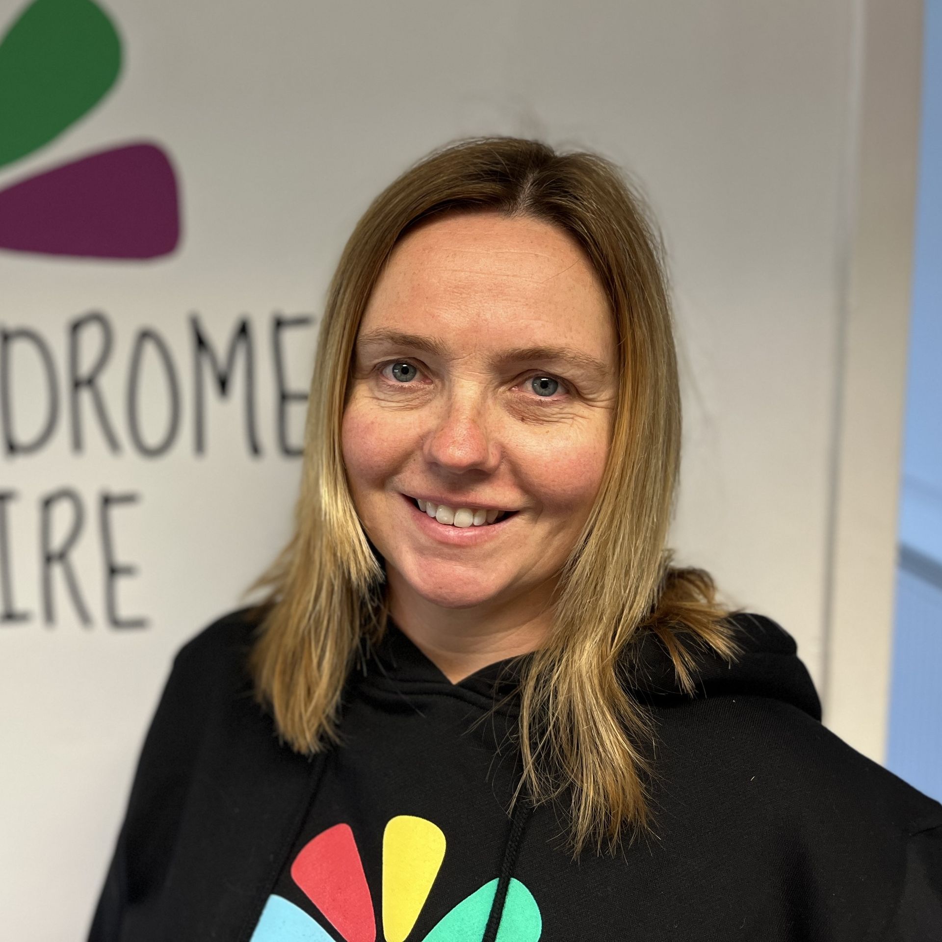 A woman in a black hoodie is smiling in front of a sign that says drome ire
