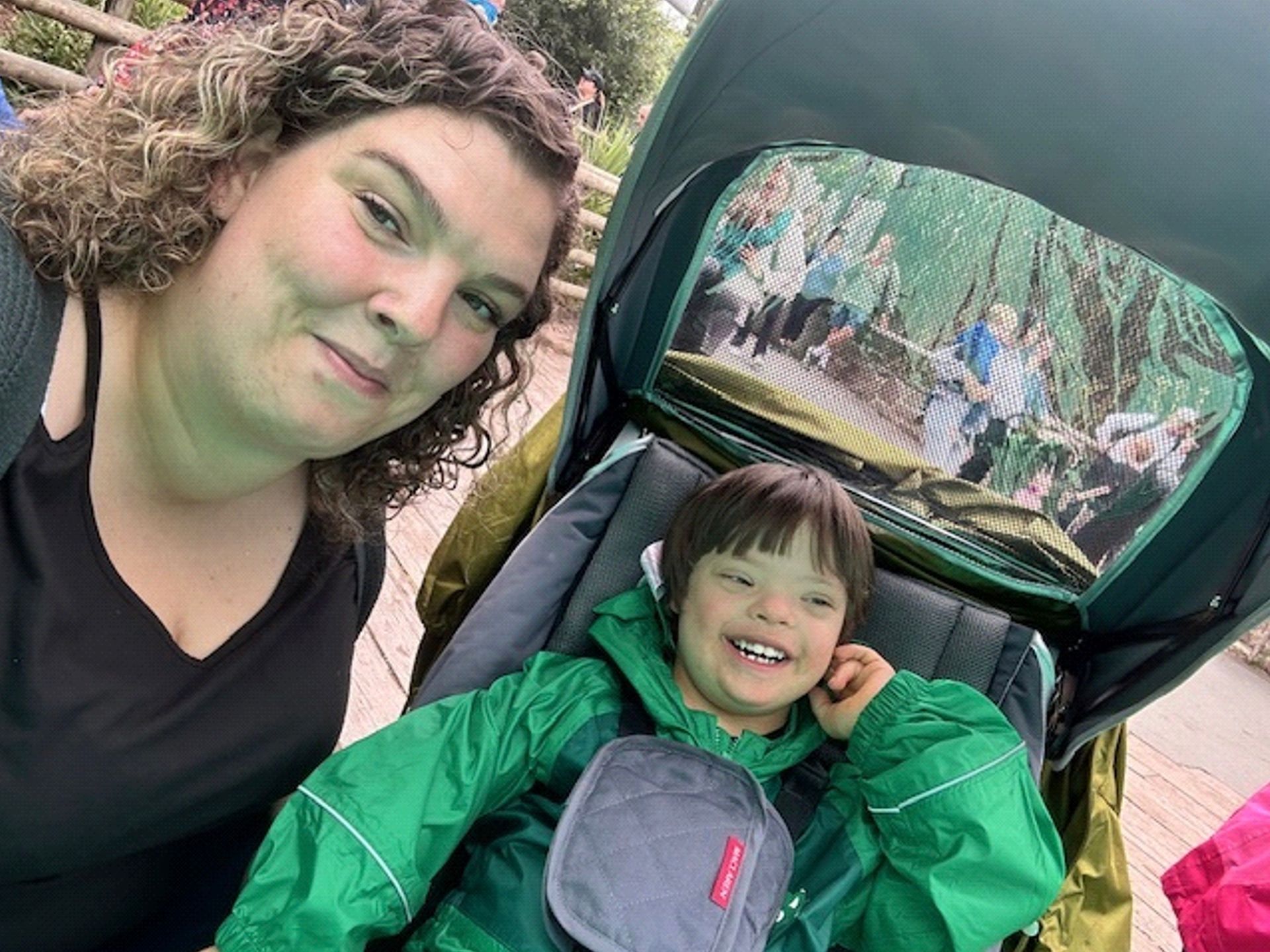 A mum crouched down next to her son with Down syndrome sat in a stroller