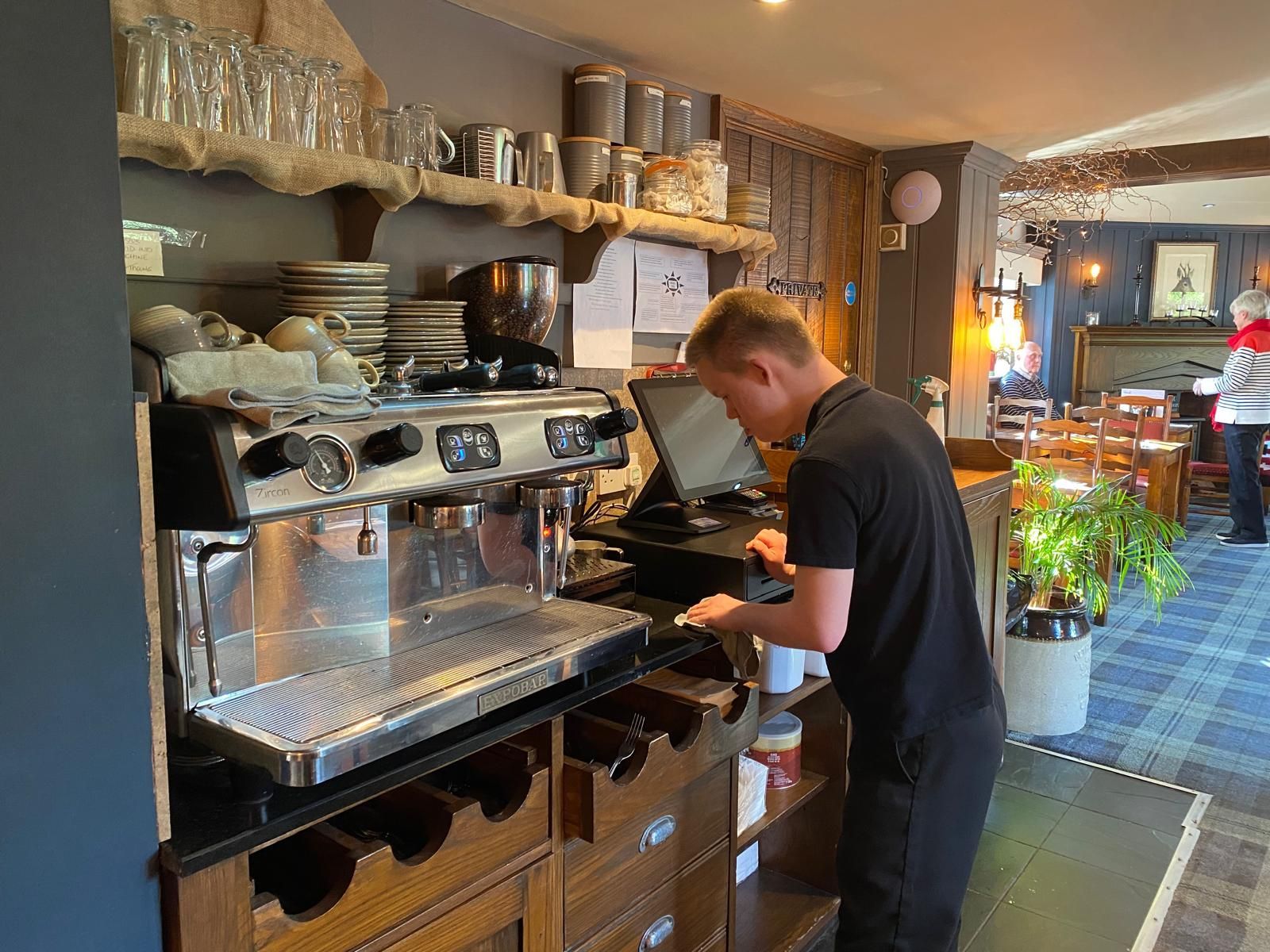 A young man with Down syndrome making and serving a coffee in a pub