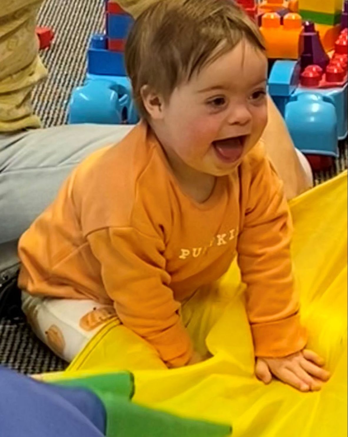 a baby wearing an orange shirt that says pumpkin is crawling on a yellow blanket