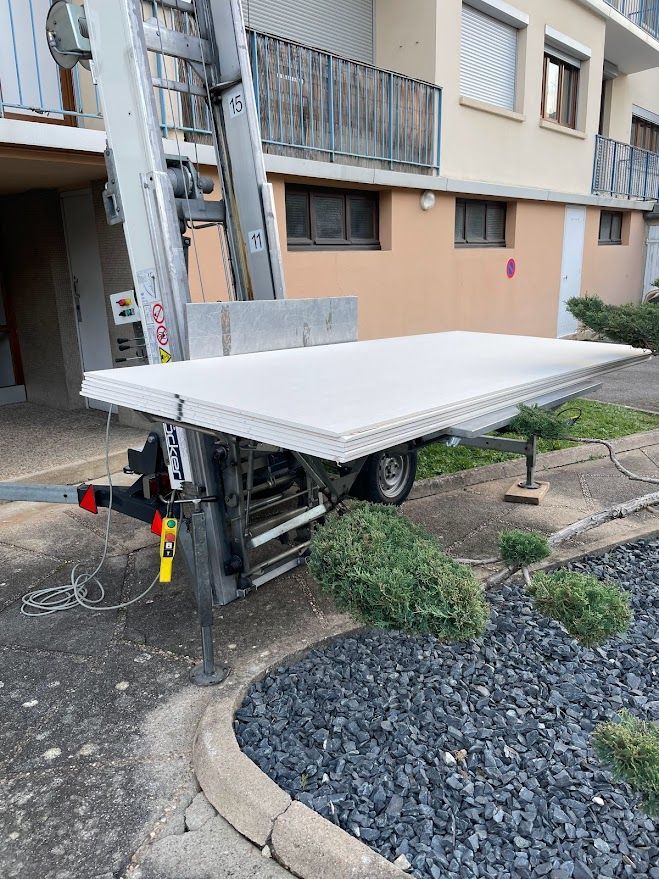 Une remorque avec une échelle attachée est garée devant un bâtiment.