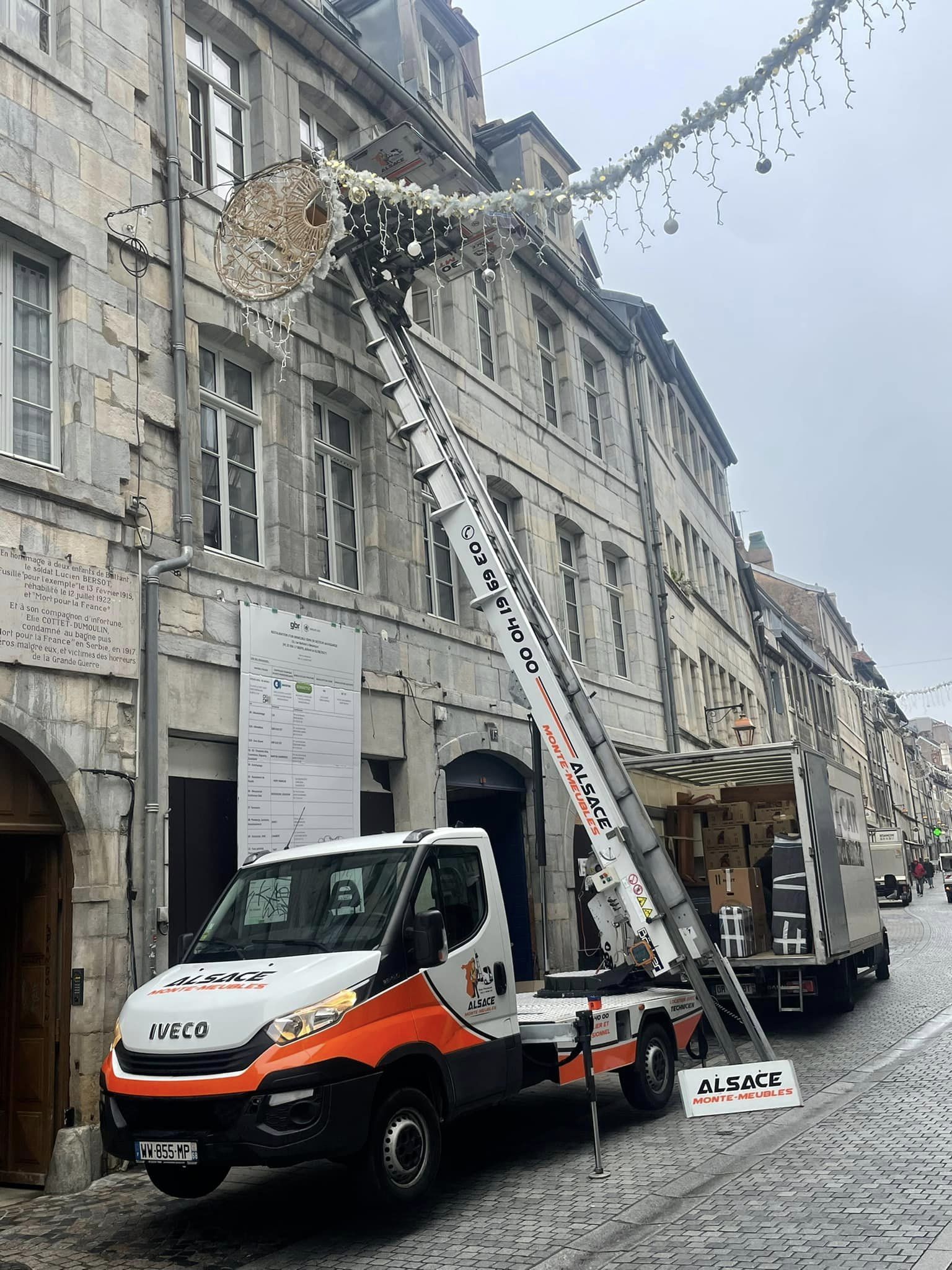 Un camion avec une échelle attachée est garé devant un bâtiment.