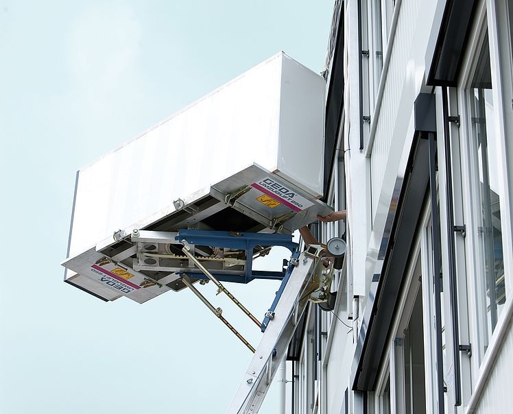 Une grande boîte blanche est soulevée jusqu'au côté d'un bâtiment