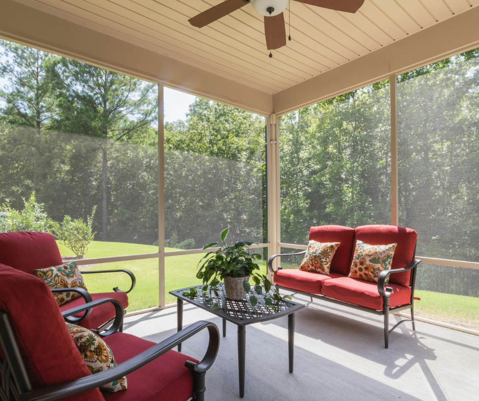 Screened-in porch with red outdoor furniture, ceiling fan, and view of trees.