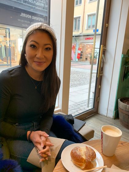 Woman in cafe, smiling, with coffee and pastry. Wearing headband, sitting by window.