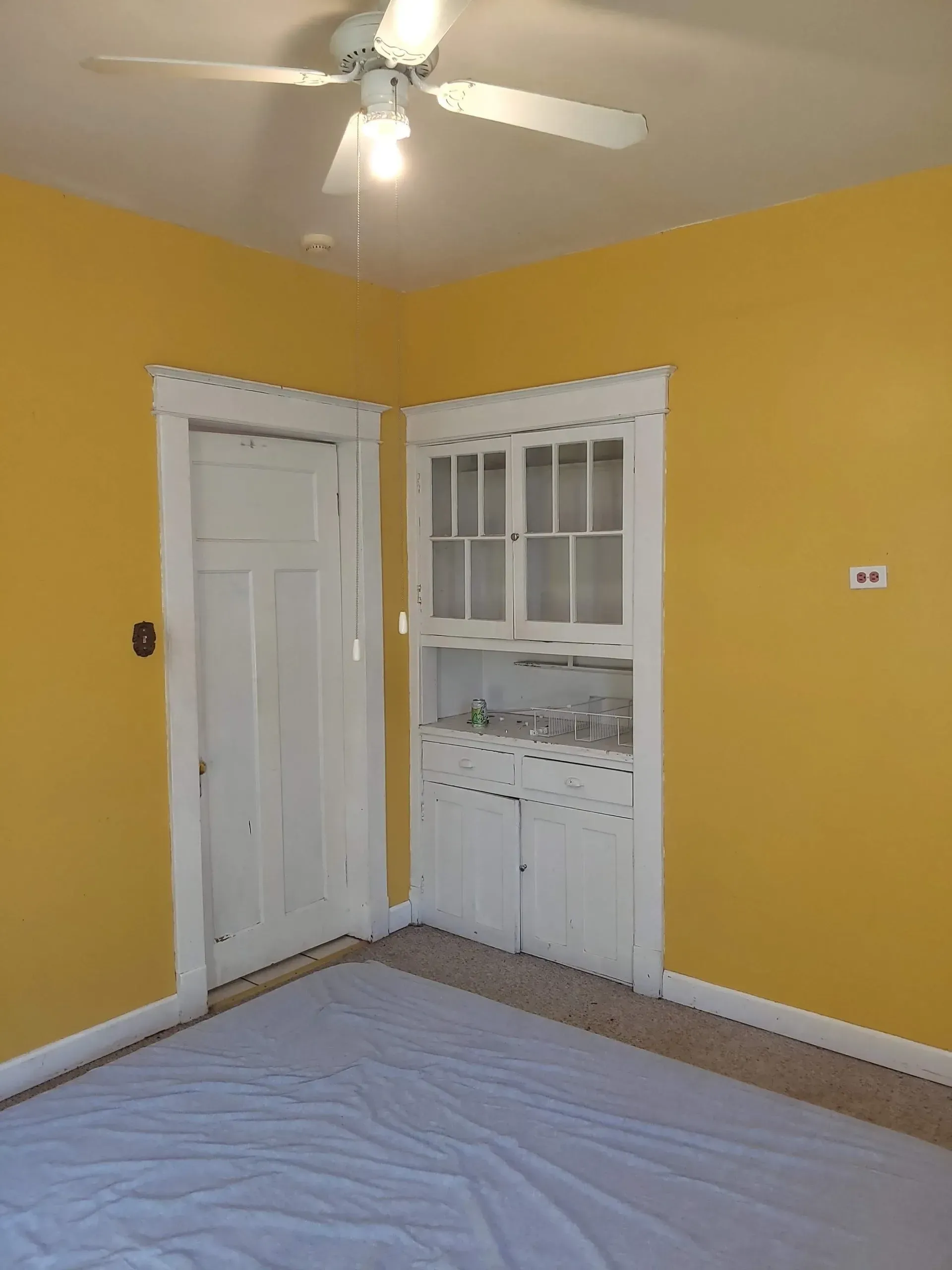 An empty room with yellow walls and a ceiling fan.