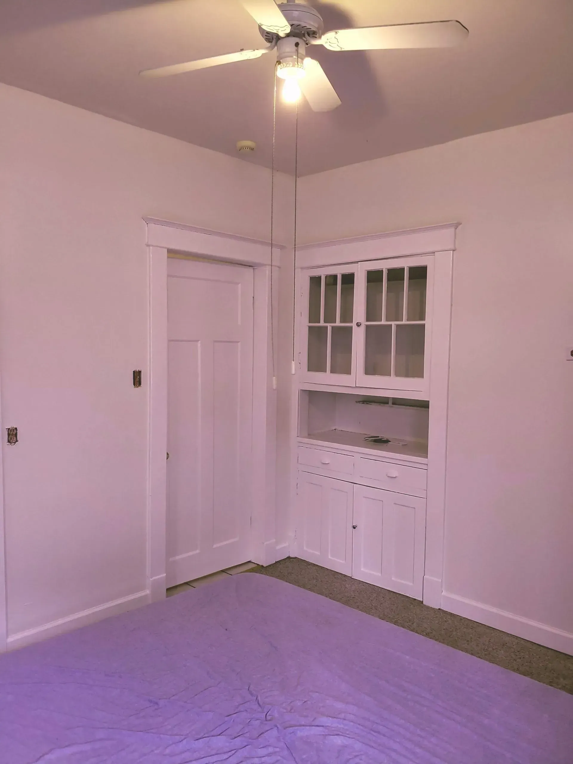 An empty room with a purple rug and a ceiling fan