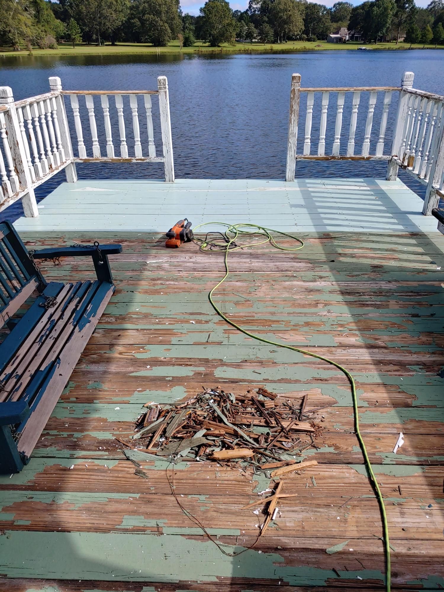 A wooden deck with a swing and a drill on it next to a lake.