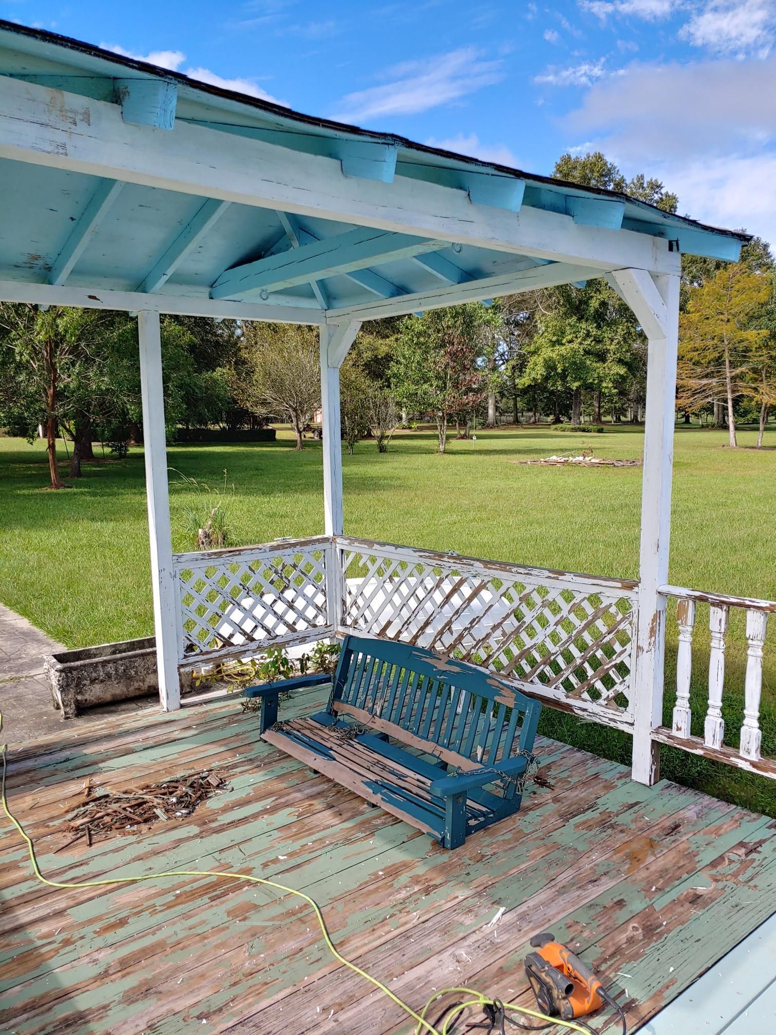 A blue bench is sitting on a wooden deck under a gazebo.