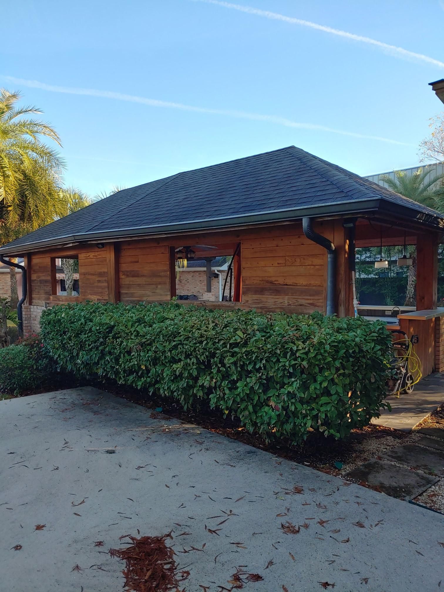 A wooden house with a black roof is surrounded by bushes.