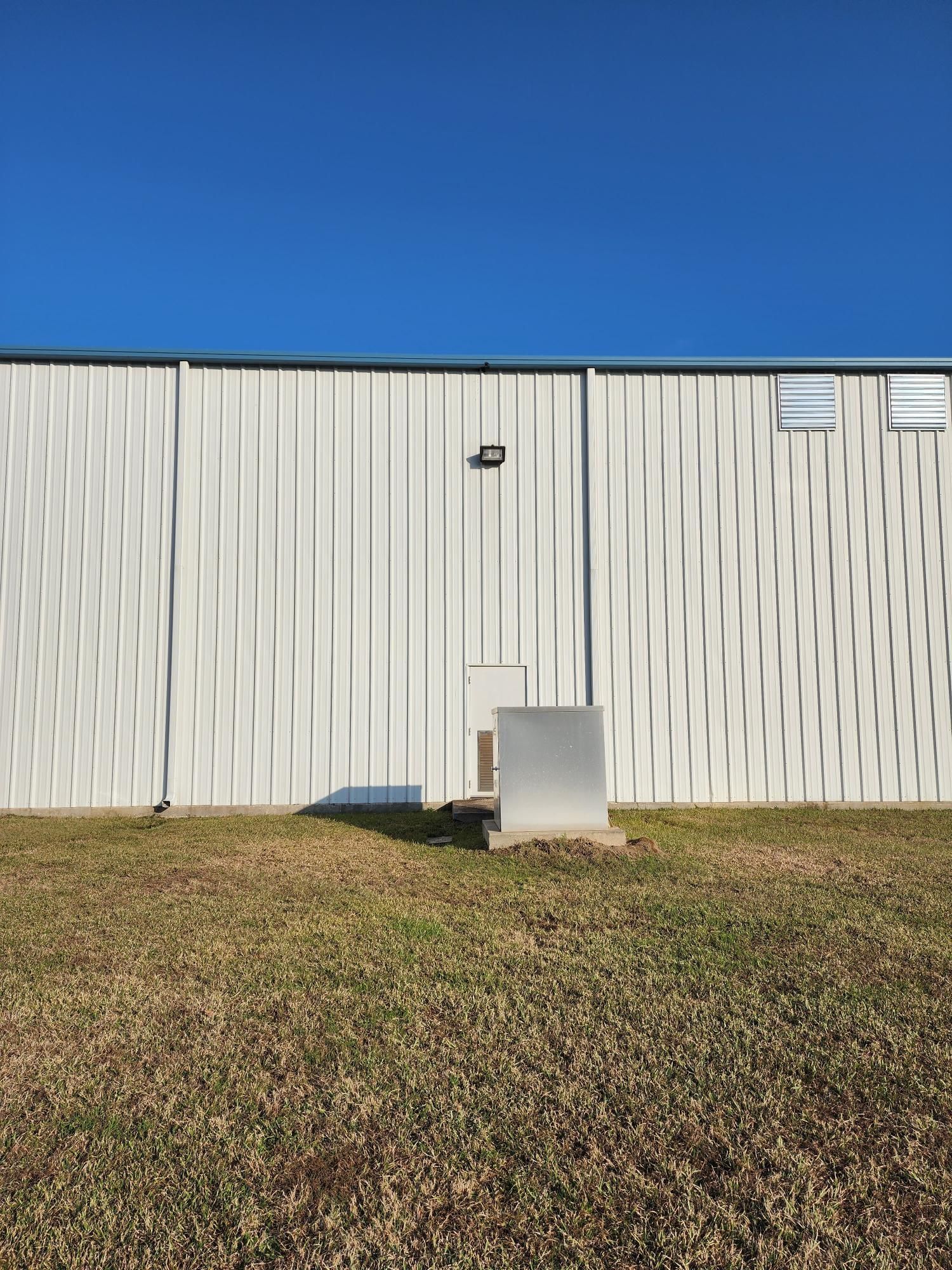 A large white building is sitting in the middle of a grassy field.