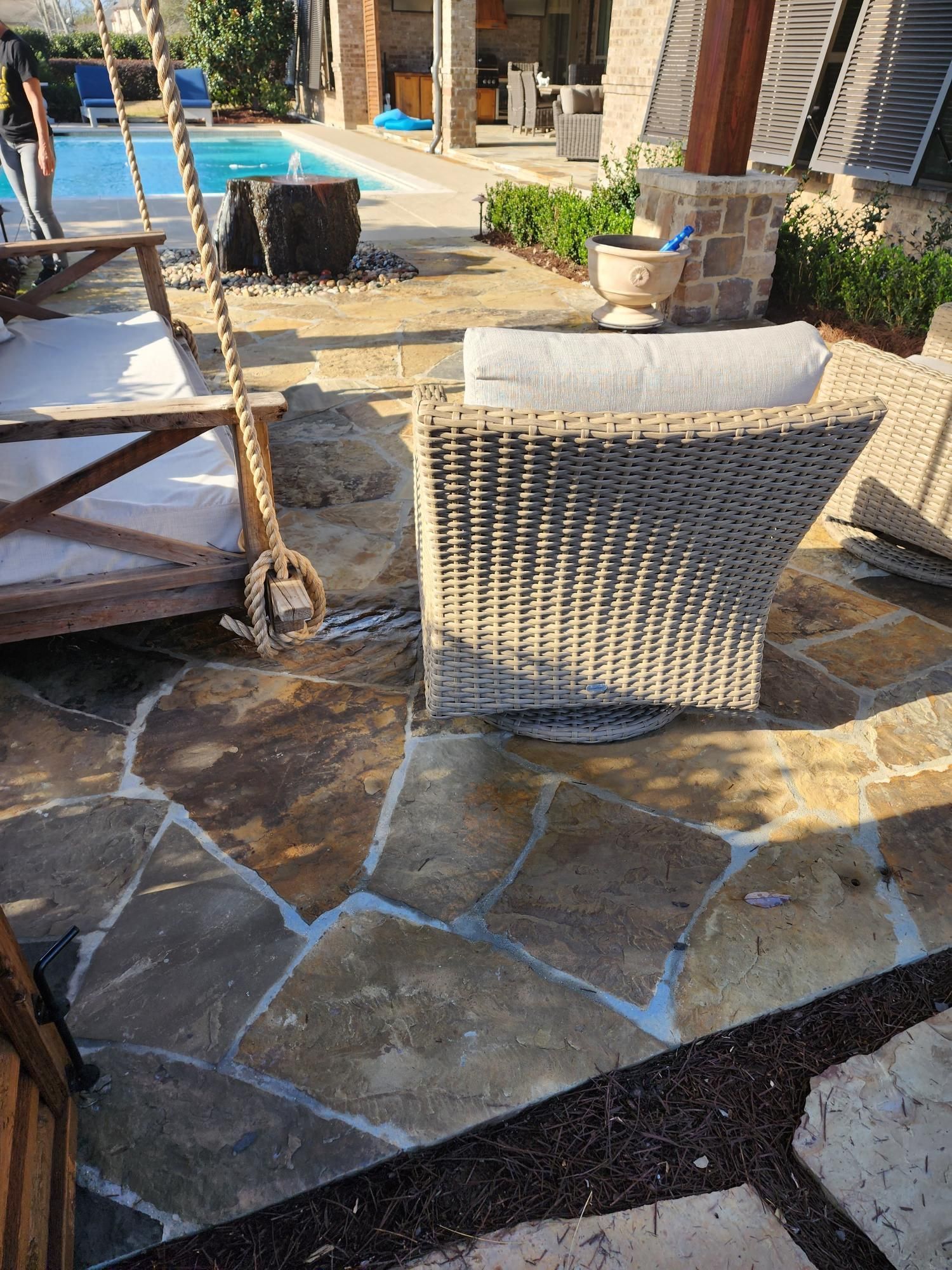 A wicker chair is sitting on a stone patio next to a swing.