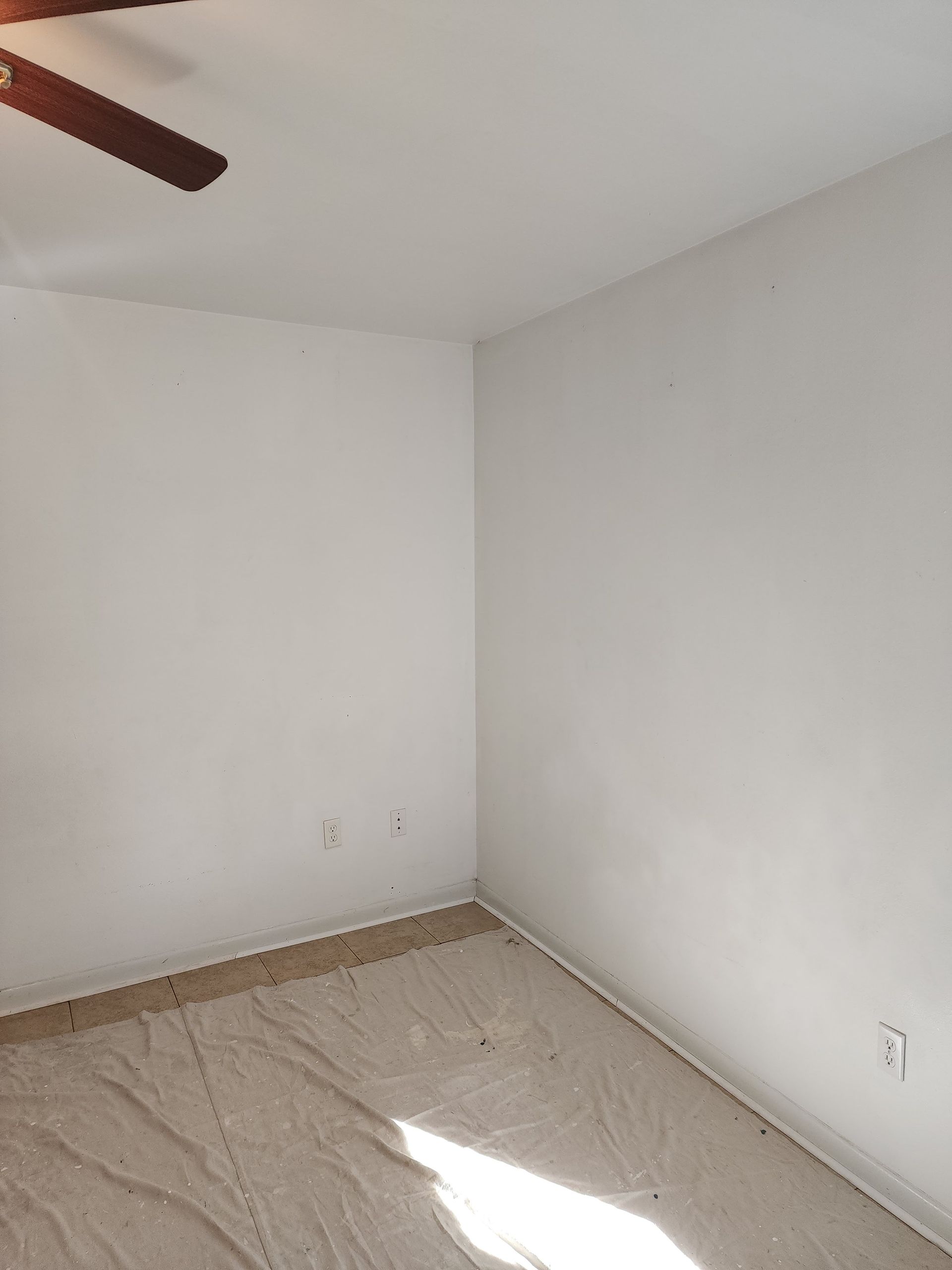 An empty room with white walls and a ceiling fan.