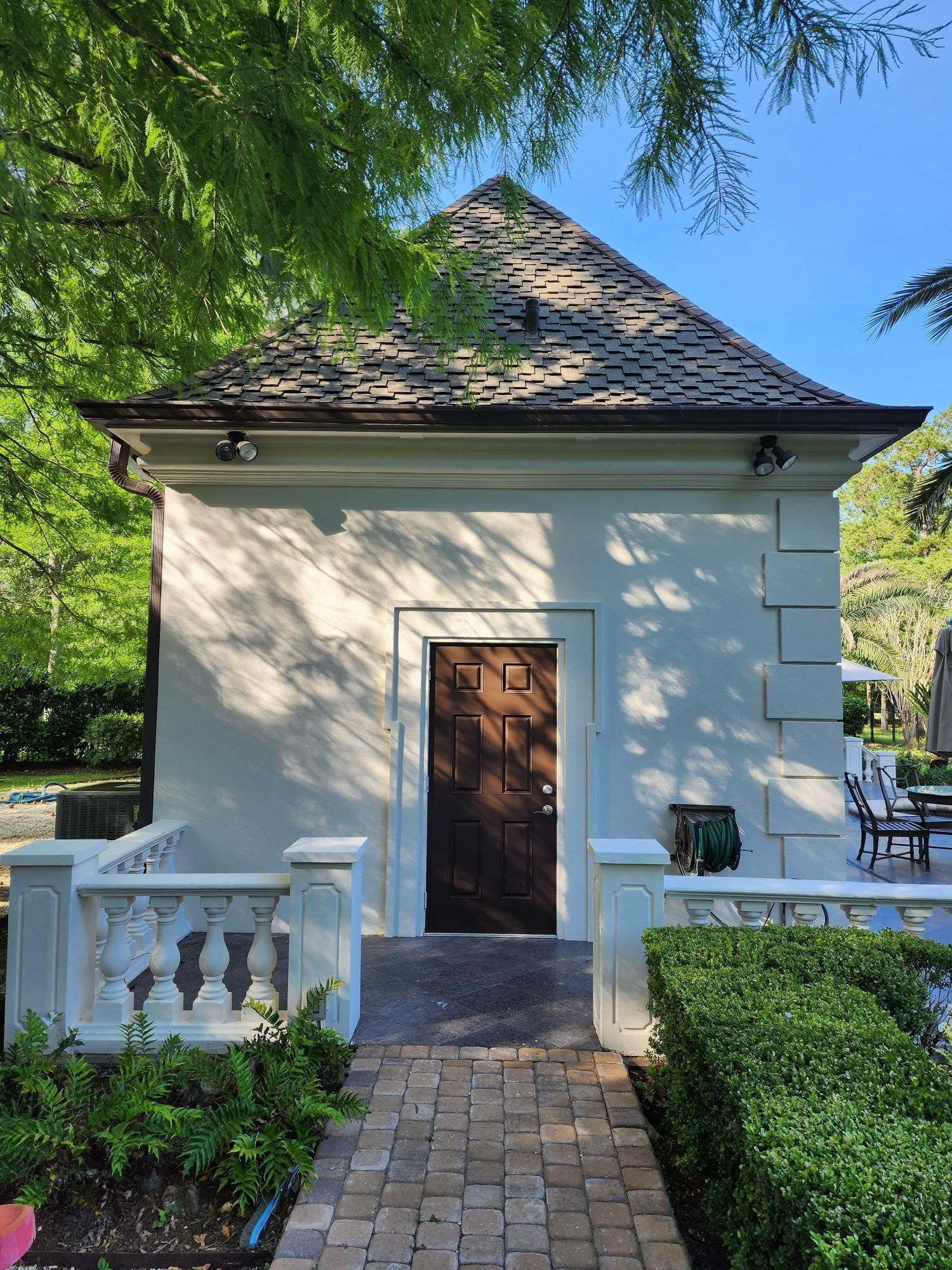 A white house with a brown door and a brick walkway leading to it.