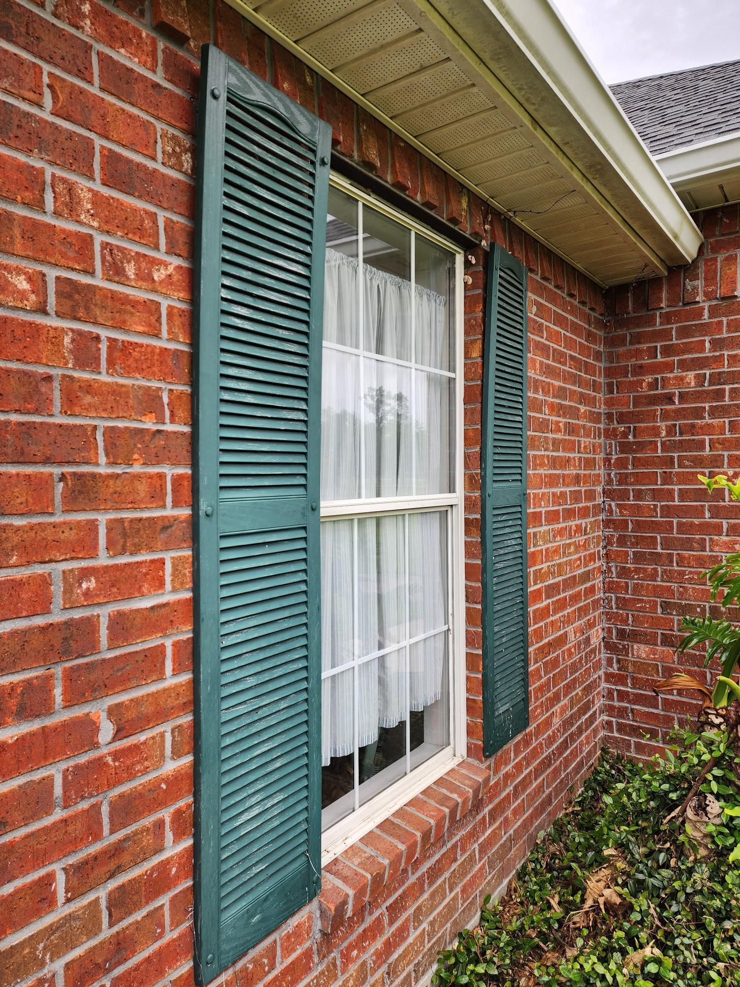 A red brick house with green shutters on the windows.
