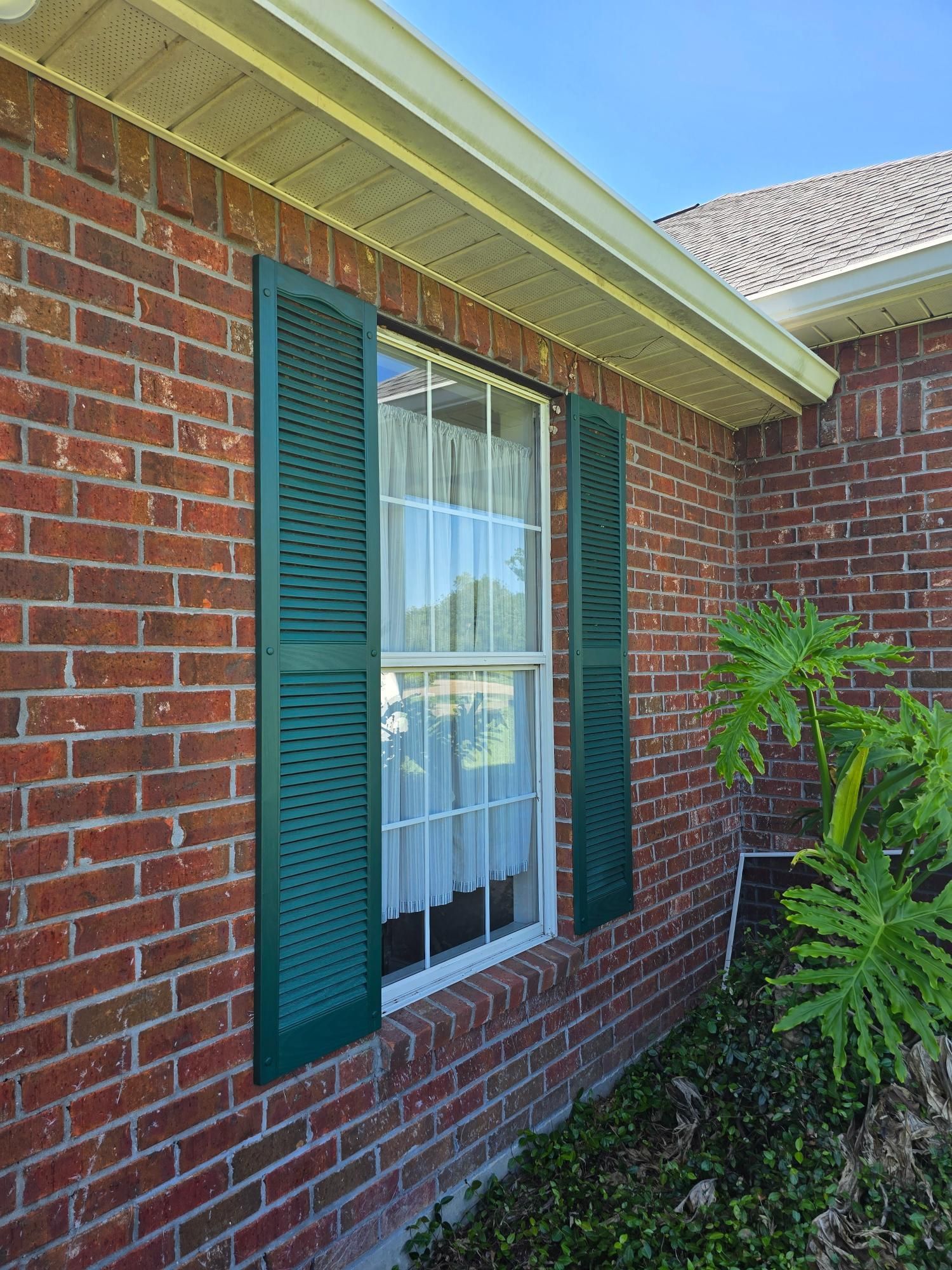 A red brick house with green shutters on the windows