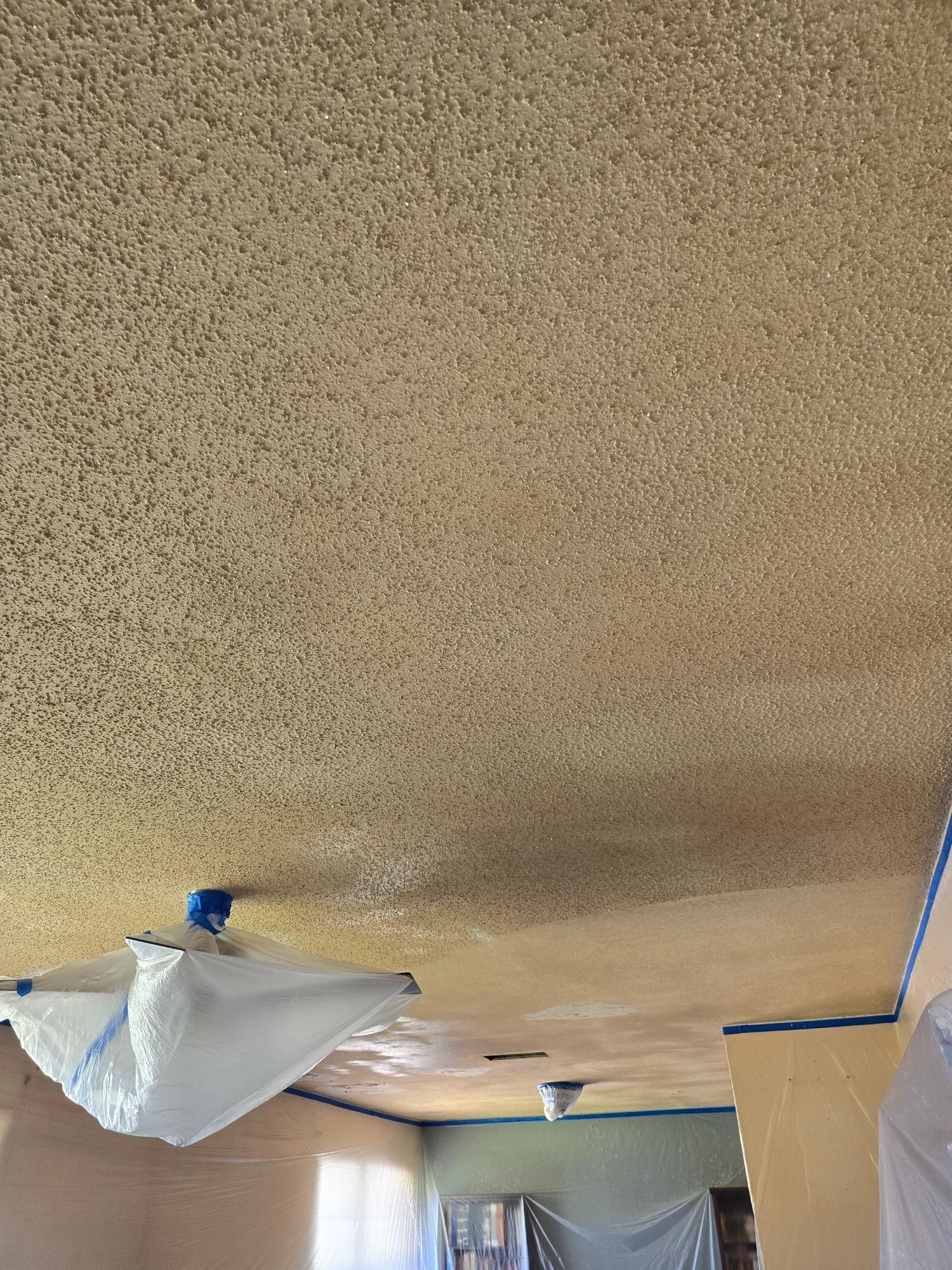 A room with a ceiling that is being painted and covered in plastic.