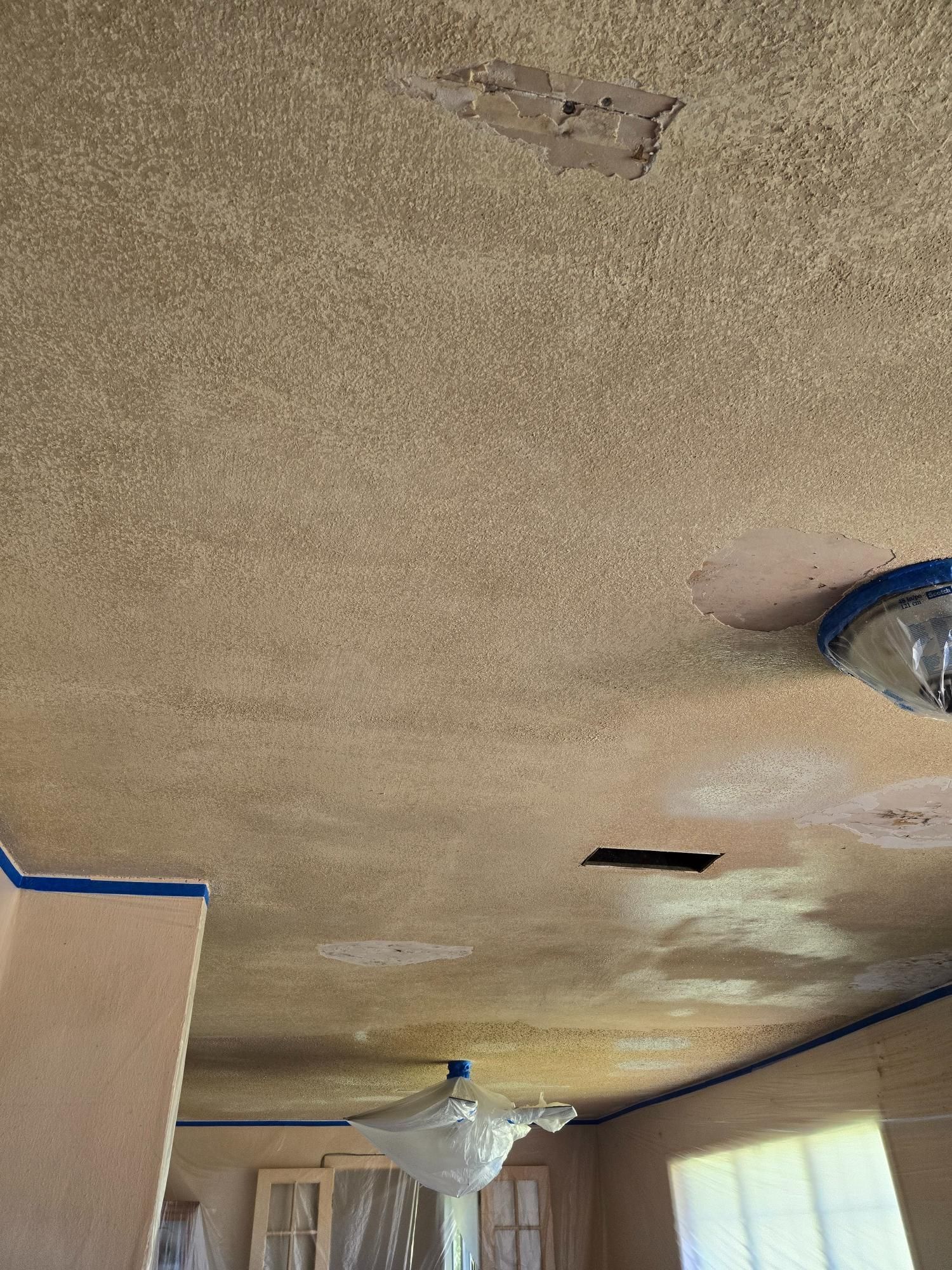 A room with a ceiling that is being painted and a ceiling fan.