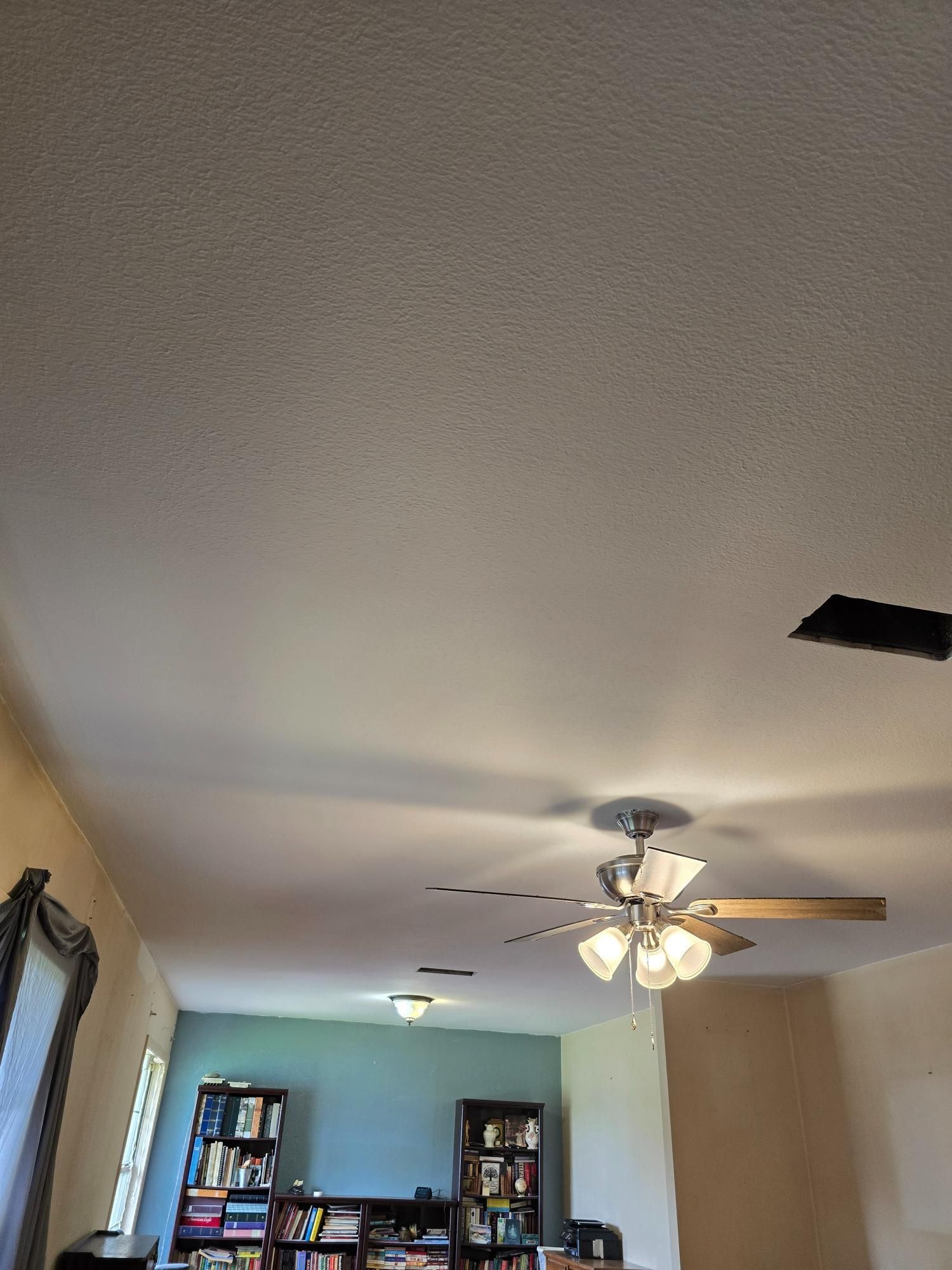A living room with a ceiling fan and a bookshelf.