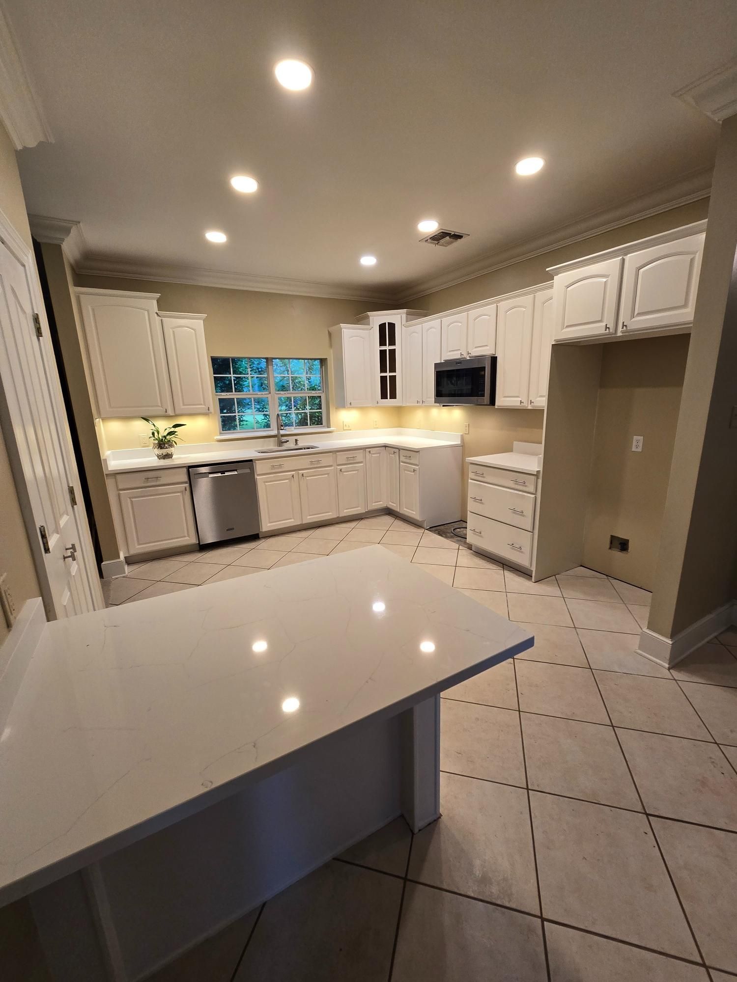 A kitchen with white cabinets , stainless steel appliances , and a large island.