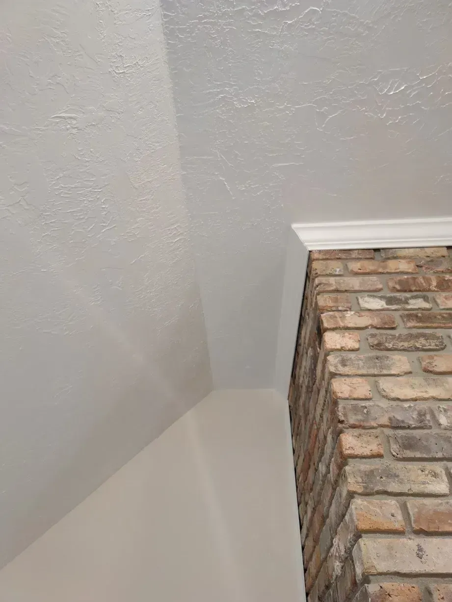 A corner of a room with a brick fireplace and a white wall.